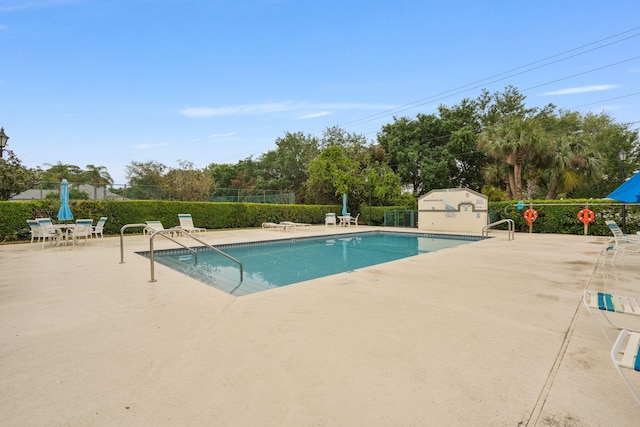 pool with an outdoor structure, fence, and a patio