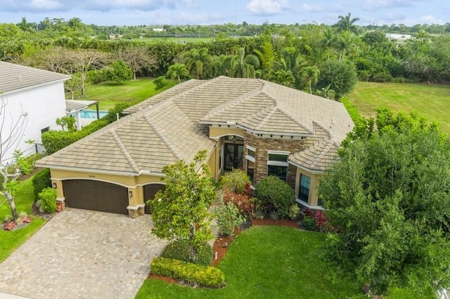 view of front facade featuring a garage, stone siding, a front lawn, and decorative driveway