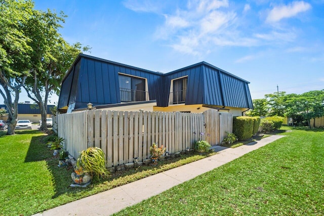 view of side of property featuring a yard, metal roof, fence, and mansard roof
