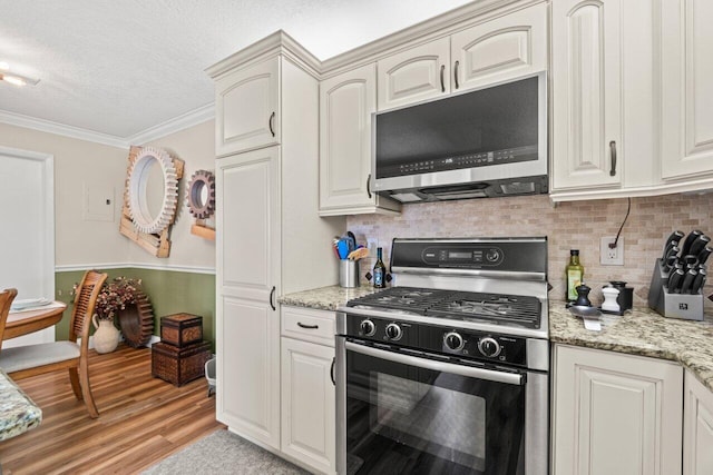 kitchen with crown molding, a textured ceiling, stainless steel microwave, gas range oven, and backsplash