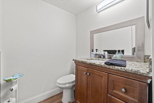 half bathroom featuring toilet, vanity, wood finished floors, and baseboards
