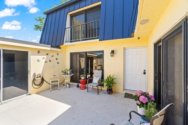 rear view of house with a patio area, metal roof, mansard roof, and stucco siding