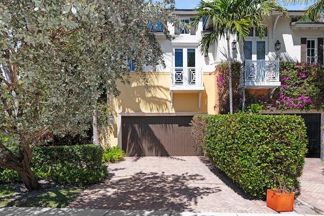 view of front facade featuring a garage, a balcony, stucco siding, and decorative driveway