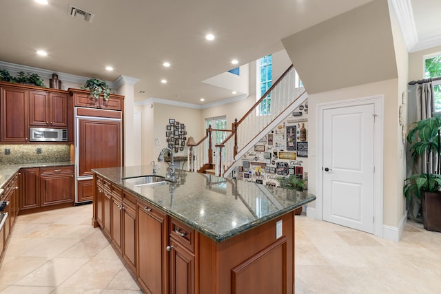 kitchen featuring paneled refrigerator, a healthy amount of sunlight, a sink, stainless steel microwave, and a kitchen island with sink