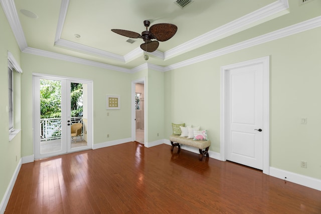 empty room with a tray ceiling, visible vents, a ceiling fan, crown molding, and wood-type flooring