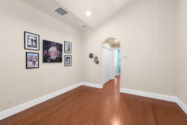 spare room featuring baseboards, visible vents, arched walkways, and dark wood finished floors