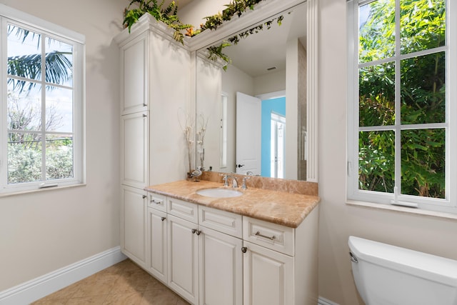 bathroom with baseboards, toilet, vanity, and a wealth of natural light