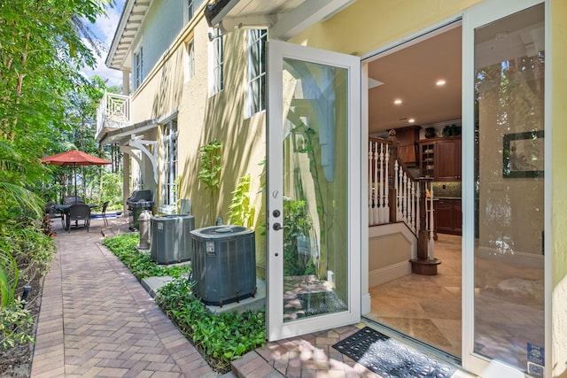 entrance to property with stucco siding, central AC unit, outdoor dining space, and a patio