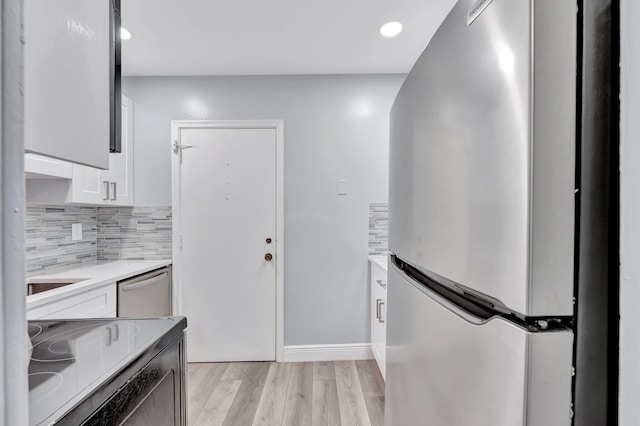 interior space featuring white cabinets, light countertops, stainless steel appliances, light wood-style flooring, and decorative backsplash