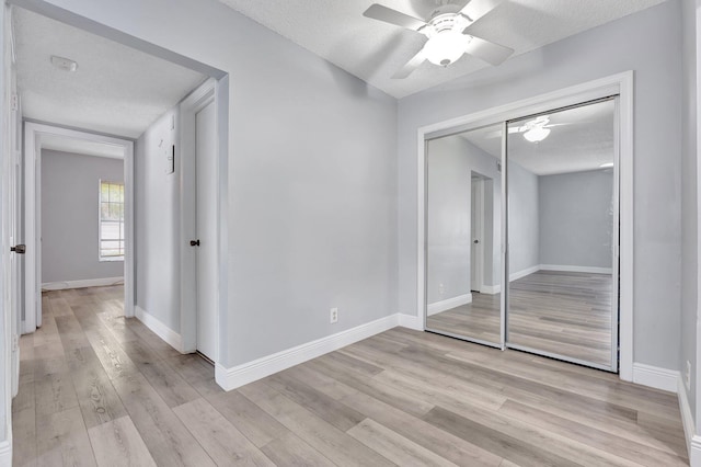 unfurnished bedroom featuring a closet, baseboards, a ceiling fan, light wood-type flooring, and a textured ceiling
