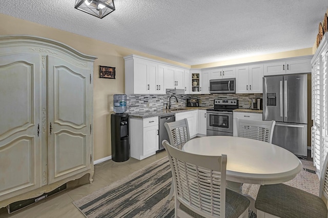 kitchen featuring a textured ceiling, appliances with stainless steel finishes, tasteful backsplash, a sink, and white cabinets