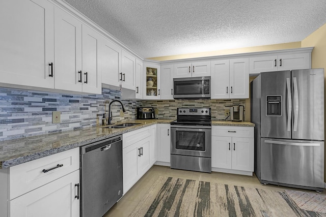 kitchen featuring glass insert cabinets, a textured ceiling, white cabinetry, a sink, and stainless steel appliances