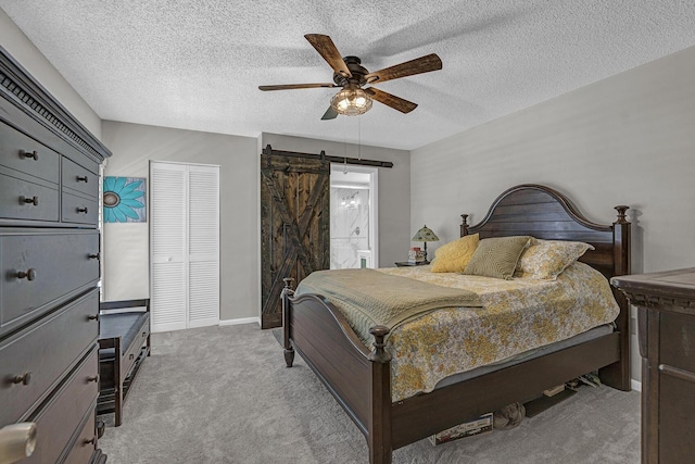 bedroom with a closet, ceiling fan, light colored carpet, a barn door, and a textured ceiling