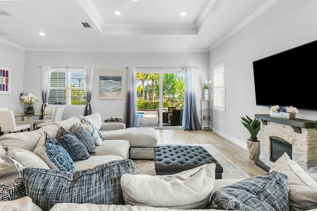 living room with a tray ceiling, baseboards, visible vents, wood finished floors, and crown molding