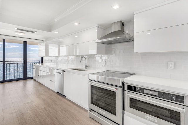 kitchen with white cabinets, wall chimney exhaust hood, stainless steel appliances, and modern cabinets
