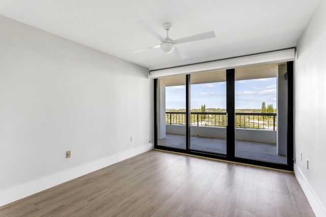 spare room featuring a wall of windows, wood finished floors, baseboards, and ceiling fan