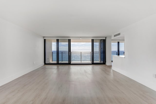 unfurnished room with a wall of windows, baseboards, wood finished floors, and visible vents