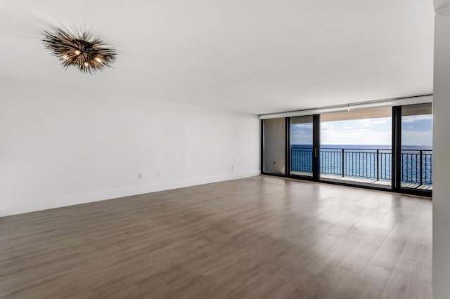 unfurnished room with a wall of windows, wood finished floors, a water view, and baseboards