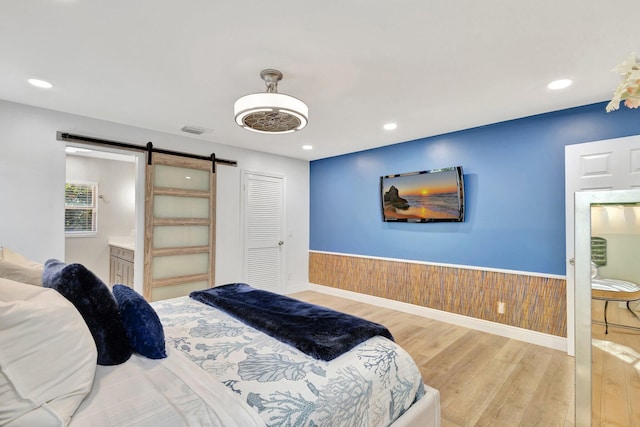 bedroom featuring recessed lighting, a barn door, wainscoting, visible vents, and wood finished floors