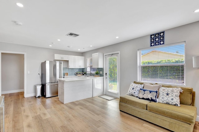 kitchen with freestanding refrigerator, tasteful backsplash, white cabinets, light countertops, and a sink
