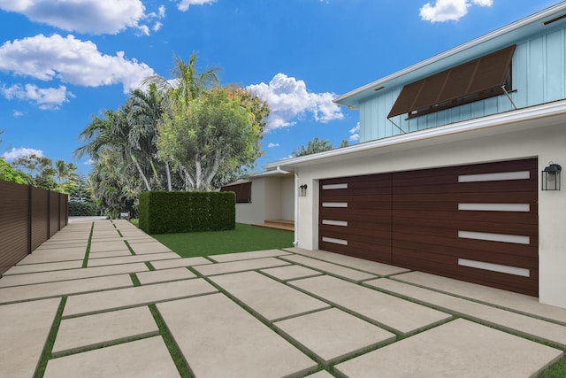exterior space featuring board and batten siding, stucco siding, driveway, and fence