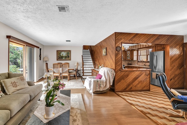 living area with a textured ceiling, visible vents, stairs, wooden walls, and light wood-type flooring