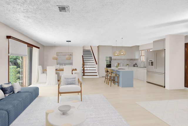 living area with stairway, a textured ceiling, visible vents, and light wood-style floors