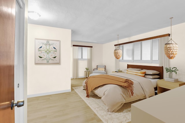 bedroom featuring baseboards, light wood finished floors, and an inviting chandelier