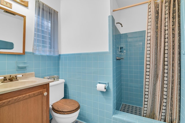 bathroom featuring toilet, a stall shower, a wainscoted wall, tile walls, and vanity