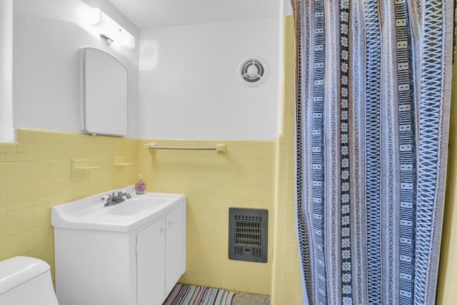 full bath with wainscoting, vanity, tile walls, and toilet