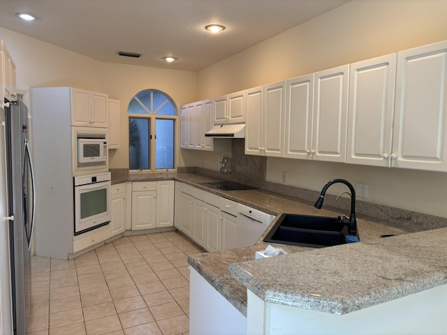 kitchen featuring white cabinets, under cabinet range hood, a sink, white appliances, and a peninsula