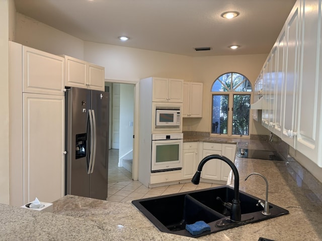 kitchen with white cabinetry, a sink, white appliances, and light tile patterned floors