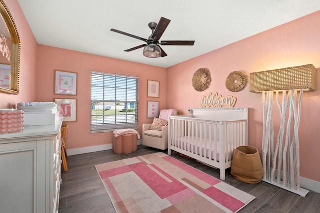 bedroom featuring ceiling fan, baseboards, a nursery area, and wood finished floors