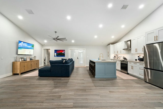 kitchen featuring ceiling fan, wall chimney range hood, visible vents, stainless steel appliances, and open floor plan