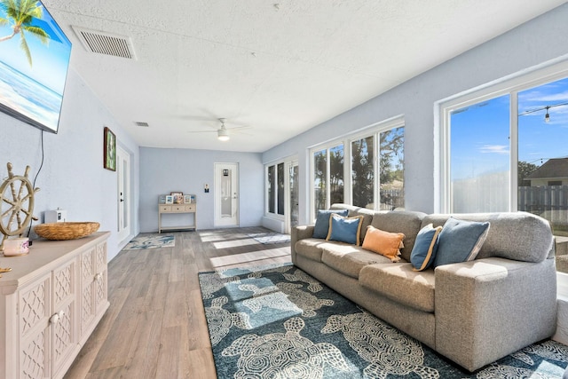 living room with light wood finished floors, visible vents, a textured ceiling, and ceiling fan