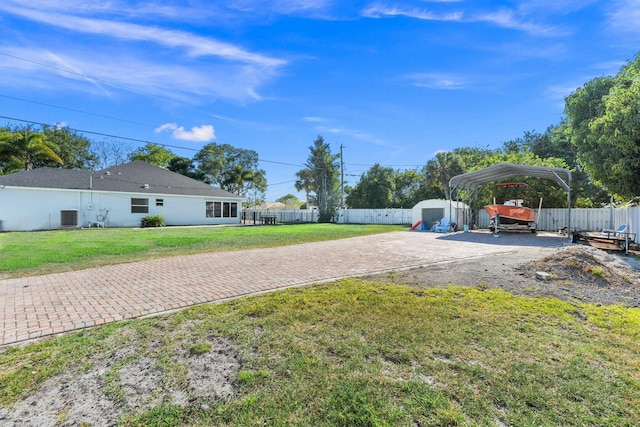 view of yard featuring a carport, driveway, fence, and a storage unit