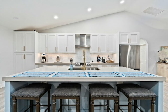 kitchen with vaulted ceiling, wall chimney range hood, freestanding refrigerator, visible vents, and decorative backsplash