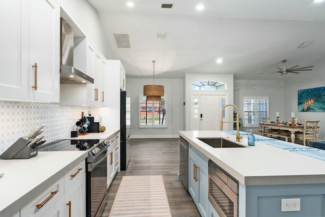 kitchen featuring visible vents, wall chimney exhaust hood, a sink, light countertops, and appliances with stainless steel finishes