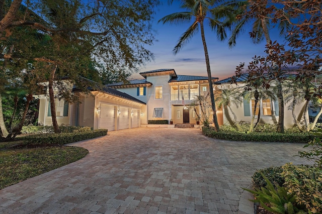 mediterranean / spanish-style home with a garage, stucco siding, decorative driveway, a balcony, and metal roof