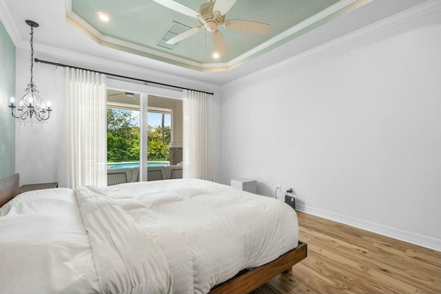 bedroom featuring wood finished floors, access to exterior, baseboards, crown molding, and a tray ceiling