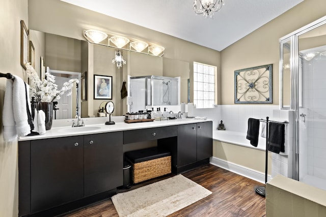 full bath with double vanity, a garden tub, a shower stall, wood finished floors, and a sink