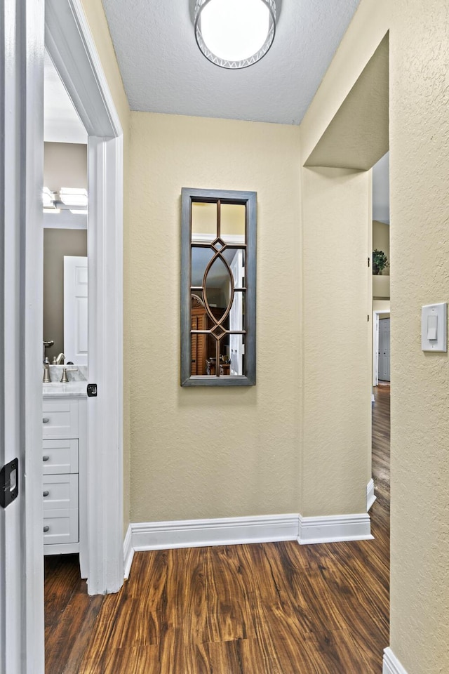 corridor with baseboards, a textured wall, and wood finished floors