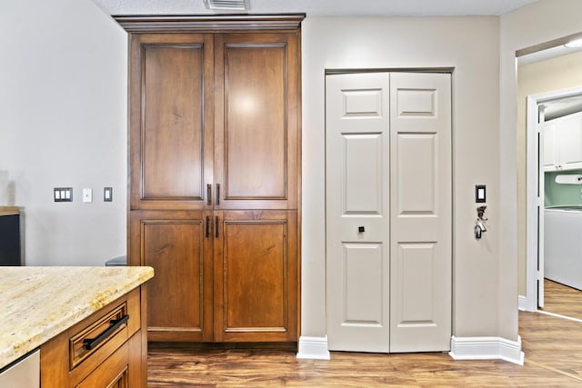 kitchen with light wood-type flooring, baseboards, washer / dryer, and light stone counters