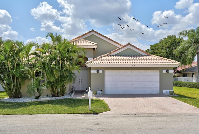 mediterranean / spanish-style house with stucco siding, an attached garage, decorative driveway, and a front yard