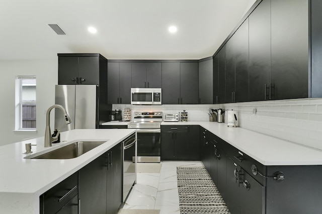 626 33rd St, West Palm Beach, FL 33407 - kitchen featuring appliances with stainless steel finishes, a sink, dark cabinetry, tasteful backsplash, and recessed lighting