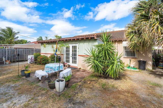 rear view of property featuring french doors, stucco siding, fence, and a tiled roof