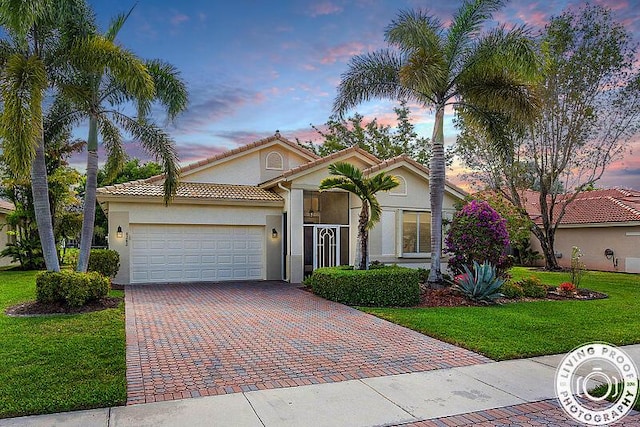 mediterranean / spanish-style house featuring a tiled roof, an attached garage, a yard, stucco siding, and decorative driveway