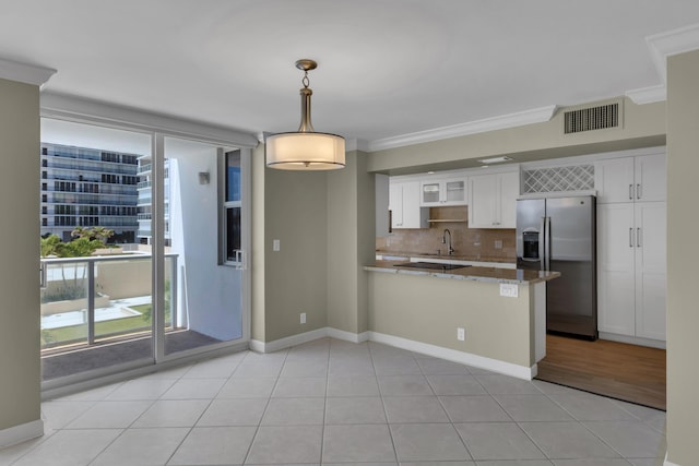 kitchen with stainless steel refrigerator with ice dispenser, a peninsula, white cabinets, ornamental molding, and tasteful backsplash