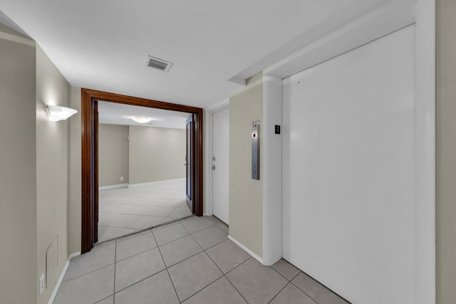 hall featuring elevator, light tile patterned flooring, and baseboards