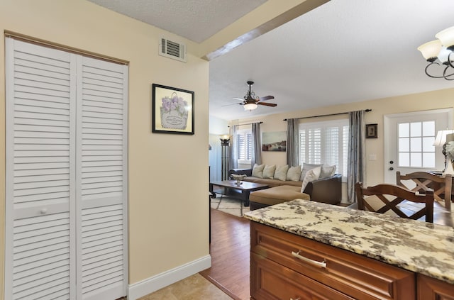 kitchen featuring a textured ceiling, brown cabinets, visible vents, baseboards, and ceiling fan with notable chandelier
